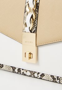 Borsa beige testurizzata con chiusura dorata, caratterizzata da un bordo con motivo a serpente e dettagli bianchi, accentuata da una catenina dorata.