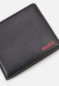 Svart läderplånbok med texturerad yta, vikbar design och röd "HUGO"-logotyp i ett hörn. Ren sömnad längs kanterna.