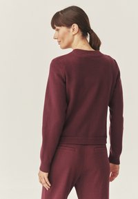 Maglione borgogna con scollo rotondo, polsini e orlo a coste. Texture morbida, design semplice, forma aderente e maniche lunghe.