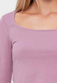 Svijetloplavi dugi rukav s okruglim izrezom. Glatka, rastezljiva tkanina s uskim krojem. Nema vidljivih uzoraka ili detalja.