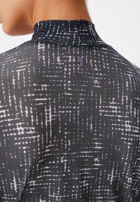 Zwarte geblokte stoffen top met een hoge kraag, voorzien van een paarse logo-tag en een textuurpatroon in witte en lavendel tinten.