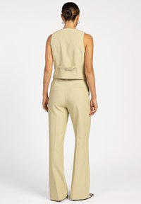 Lichtbeige op maat gemaakte gilet en wijde broek van gestructureerd materiaal. Het gilet heeft een strikdetail aan de achterkant en minimale naden.