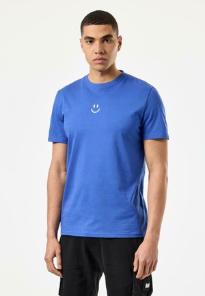 Blaues T-Shirt mit kurzen Ärmeln aus Baumwolle; verfügt über ein kleines weißes lächelndes Gesicht-Logo auf der Brust. Glatte Textur, normale Passform.