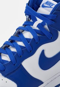 Zapatillas altas de Nike con un diseño de cuero azul y blanco, con cordones azules y un destacado logo de swoosh azul.