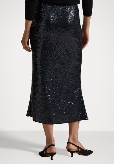 Marineblaue, mit Pailletten besetzte Midi-Rock mit einem ausgestellten Saum und strukturiertem Oberflächenmaterial. Getragen mit schwarzen High Heels, die eine elegante Passform an der Taille zeigen.