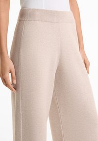 Beige, laza szárú nadrág puha, texturált anyagból készült, bordázott derékrésszel. Az oldalsó részletek mélységet adnak a sima felületnek.