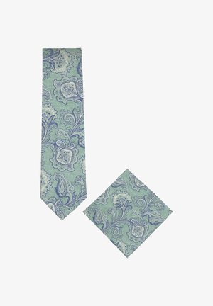 Cravate verte à motif paisley et pochette assortie pliée avec des motifs floraux bleus et blancs sur fond blanc.