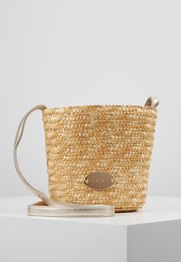 Borsa a secchiello in paglia intrecciata di colore naturale con tracolla argentata lucida e una piastra metallica elegante. Forma rotonda, superficie testurizzata.