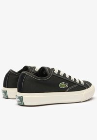 Sneaker nere in tela con lacci bianchi, suole in gomma e logo Lacoste verde. Presentano cuciture bianche e una finitura in tessuto texturizzato.