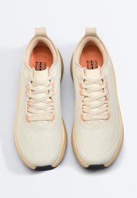 Paire de baskets athlétiques crème avec des touches pêche clair, semelles beiges et intérieurs rembourrés, vues de dessus sur fond blanc.