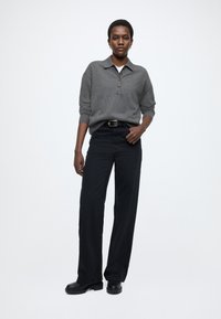 Pulover gri cu guler și nasturi, asortat cu pantaloni largi negri și cizme negre masive, prezentând un design casual și modern.