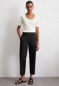 Witte, kortekraag t-shirt met korte mouwen, gecombineerd met zwarte, hooggewaiste broeken en zwarte sandalen met een gouden gespaccent.
