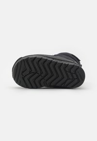 Svart Adidas stövlesula med zigzag mönster, synlig varumärkeslogotyp nära hälen och vadderad övre del mot en enfärgad vit bakgrund.