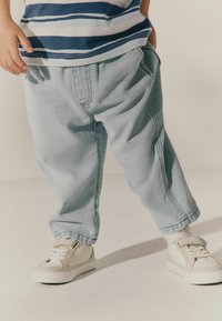 Ljusblå denimbyxor med lös passform, som har sidofickor och en något skrynklig yta, i kombination med vita sneakers och grå detaljer.