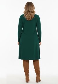 Robe longue à manches longues de couleur verte, en tissu doux, au design A-line. Associée à des bottes marron texturées jusqu'aux genoux avec des talons block.