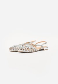 Sandales plates tissées en argent avec un design ouvert, présentant une sangle autour du talon et un accent métallique sur la semelle.