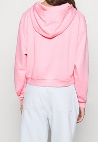 Rosa kortärmad hoodie med dragsko i huvan, ribbade ärmslut och nederkant, i kombination med ljusblå högmidjade byxor. Slät tygkvalitet.