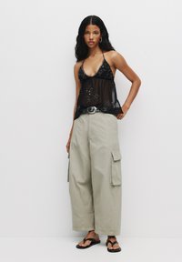 Top halter trasparente nero con dettagli di perline, abbinato a pantaloni cargo larghi di colore khaki chiaro e sandali con infradito neri.
