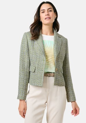 Cropped green tweed jacket with a textured pattern, two front pockets, and a single button closure, worn over a light graphic t-shirt.