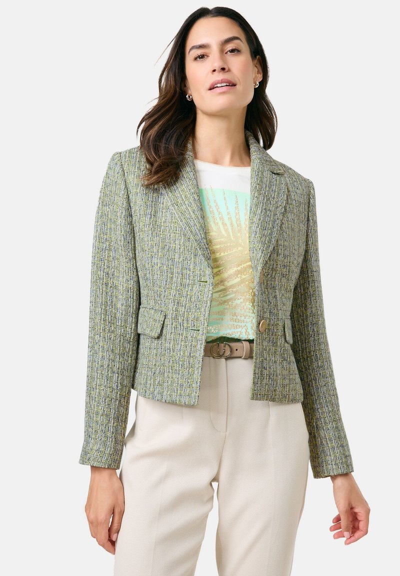 Cropped green tweed jacket with a textured pattern, two front pockets, and a single button closure, worn over a light graphic t-shirt.