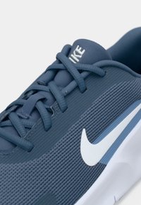 Chaussure de sport bleue avec tige en mesh, motifs texturés, logo blanc et lacets. Comprend une semelle rembourrée et des accents subtils en bleu clair.