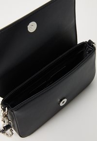 Zwarte leren schoudertas met klep open, die de interieurcompartimenten en zilveren magnetische drukknoop sluiting toont.