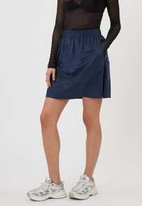 Jupe bleu marine avec taille élastique, deux poches latérales, texture lisse, coupe au niveau du genou, associée à des chaussures de sport grises.