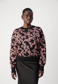 Črna majica s dolgimi rokavi vsebuje rožnato cvetlični vzorec, rebrast okrogli ovratnik in manšete. V kombinaciji z črno krilom.