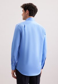 Camicia azzurra a maniche lunghe con una trama liscia, polsini con bottone, pieghe sulle spalle e colletto classico. Vestibilità su misura con orlo curvato.