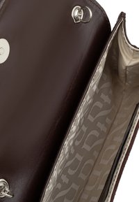 Brązowa skórzana torebka o gładkim wykończeniu, z jasnym wzorzystym wnętrzem i zapięciem na zatrzask ze srebrnymi akcentami.