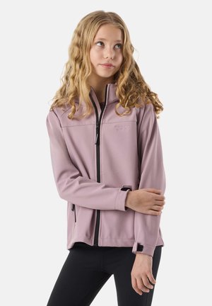 Adolescente aux cheveux blonds ondulés portant une veste zippée violette claire et des leggings noirs, regardant légèrement sur le côté.