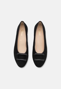 Ballerines en daim noir avec un bout arrondi et un accent de nœud noir proéminent sur le devant. L'intérieur est doublé de beige.