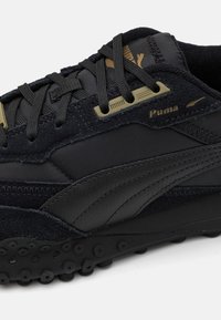 Black sneaker featuring a mix of suede and nylon materials, with a textured rubber sole and notable Puma branding.