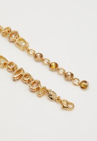 Gold-toned bracelet featuring oval and rectangular faceted gemstones in shades of amber and light yellow, connected by linked segments and a lobster clasp.