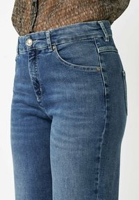 Blaue Jeans aus Denim mit taillierter Passform, mittlerem Bund und dezentem Stitching. Verfügt über fünf Taschen und silberne Metallakzente.