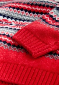 Punane kudumine sviiter, millel on fair isle muster valge, halli ja mereväe sinise värviga. Ribitud varrukad ja ääred lisavad tekstuuri. Pehme, soe villane materjal.