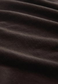 Nærbillede af blødt, mørkebrunt stof med bløde folder og en fin, glat struktur.