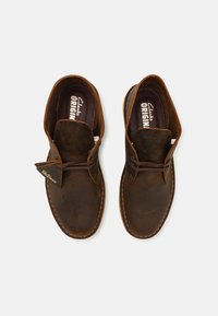 Braune Lederschuhe mit glatter Oberfläche, runder Zehenpartie, Schnürdesign und sichtbarem Nähen. Verfügt über ein Logo-Tag an der Seite.