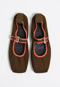 Zapatos de lona marrones con acentos naranjas y una correa con hebilla. Forma suave y redondeada con una plantilla interior negra texturizada.