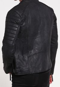 Giacca in pelle nera con spalle trapuntate, finitura elegante e cerniere laterali. Il design è aderente con una silhouette slanciata.