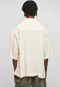 Chemise crème à manches courtes avec une coupe décontractée, présentant un léger éclat, des détails de couture contrastants et un design d'empiècement au dos.