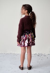 Maroon knitted sweater, sequined pink and purple skirt with glossy texture, and brown shoes. Child standing sideways with curly hair.