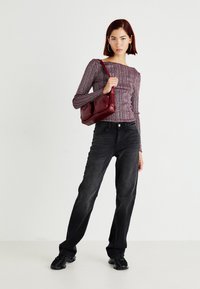 Long-sleeve, fitted, ribbed top in burgundy with ruching. Worn with high-waisted black jeans and a maroon handbag. Black sneakers.