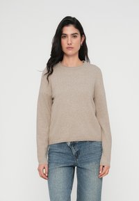 Μπεζ πουλόβερ με στρογγυλή λαιμόκοψη, μακριά μανίκια και άνετη εφαρμογή. Το υλικό φαίνεται μαλακό και υφή, με ελάχιστα ραφές.