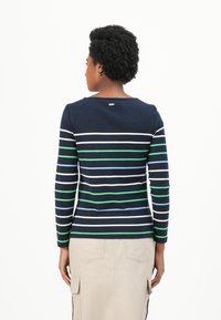Langsleeve donkerblauwe top met horizontale strepen in groen, blauw en wit. Heeft een ronde halslijn en een lichte curve aan de zoom.