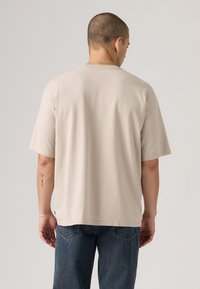 Beige bomulls t-skjorte med korte ermer og rund hals. Har avslappet passform og glatt tekstur, vist fra ryggen.