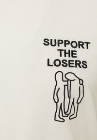 Biała koszulka z czarnym haftowanym napisem "WSPIERAJ PRZEGRANYCH" oraz trzema stylizowanymi postaciami w prostym stylu rysunku liniowego.