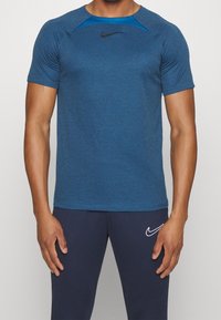 Camiseta deportiva azul de manga corta, con tejido que absorbe la humedad, cuello redondo y logotipo negro de Nike en el pecho. Presenta un diseño texturizado.