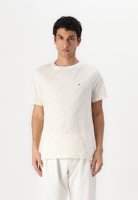 Balta īsām piedurknēm T-kreklu ar teksturētu ģeometrisku rakstu bēšā krāsā. Apaļas kakla dizains. Akcentēts logo uz krūtīm.