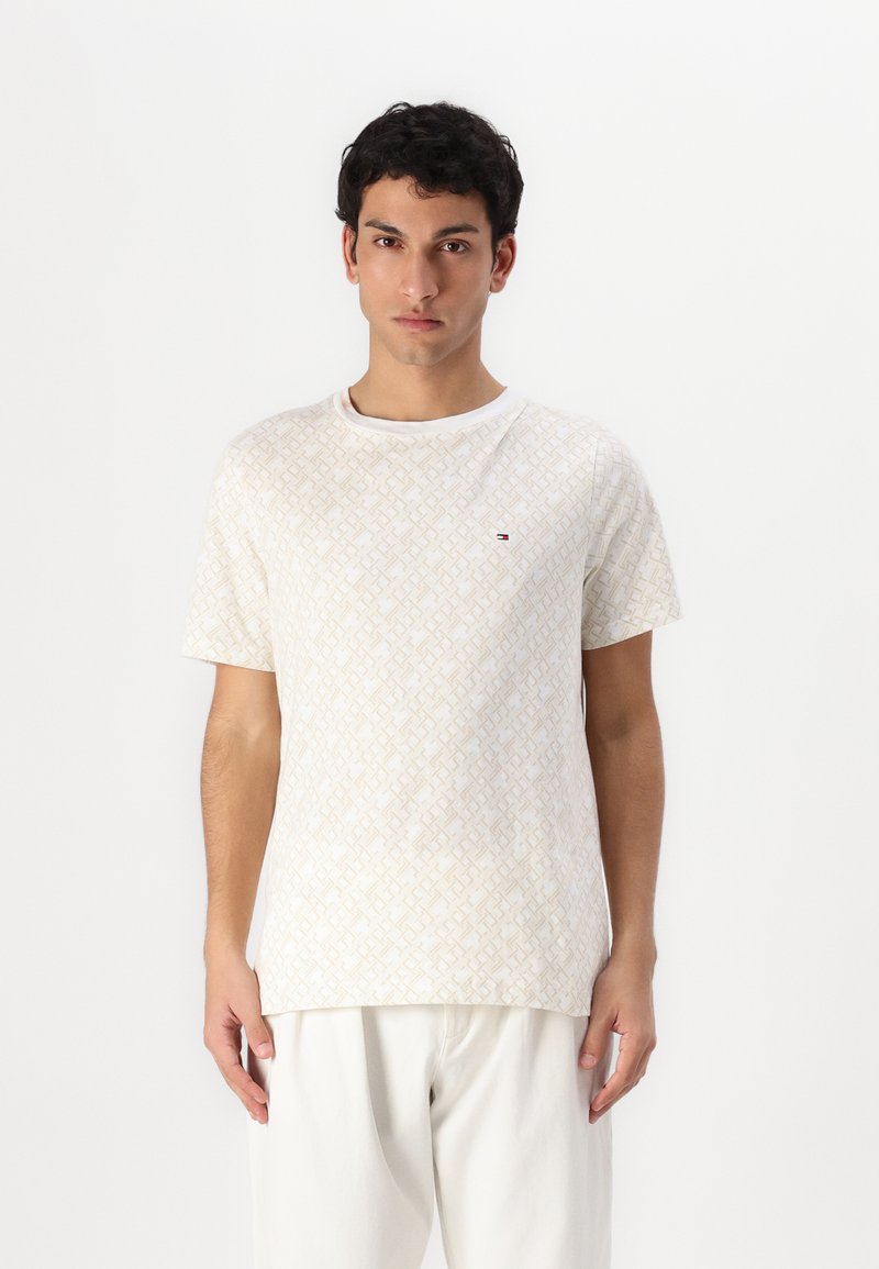 Balta īsām piedurknēm T-kreklu ar teksturētu ģeometrisku rakstu bēšā krāsā. Apaļas kakla dizains. Akcentēts logo uz krūtīm.